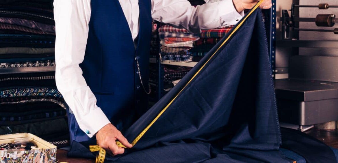 Tailor measuring navy fabric with a yellow tape measure